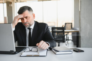 man sitting at desk in front of laptop with a frustrated face