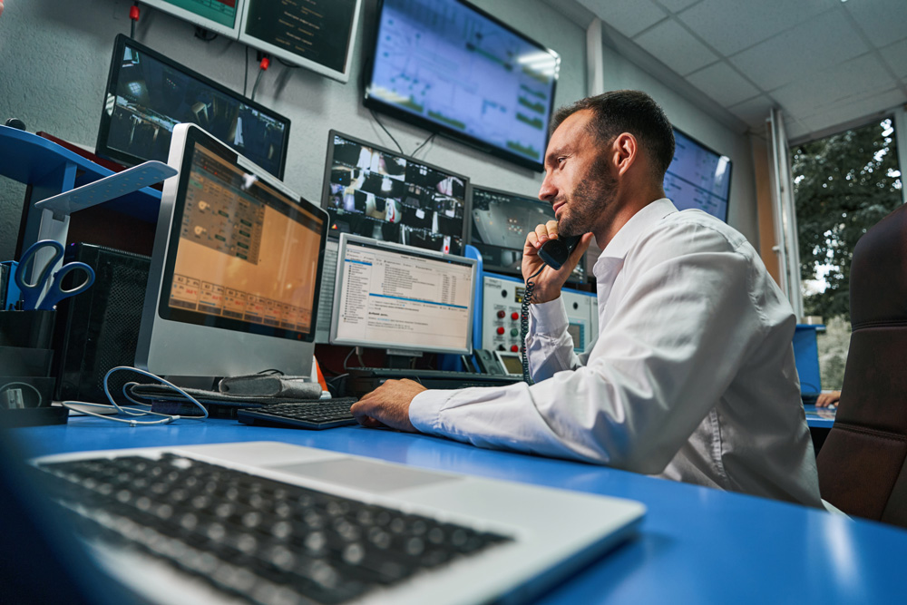 man sitting at desk surrounded by computers, keyboards, and monitors while on the phone.