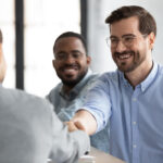 Three men meeting at a conference table with two men shaking hands