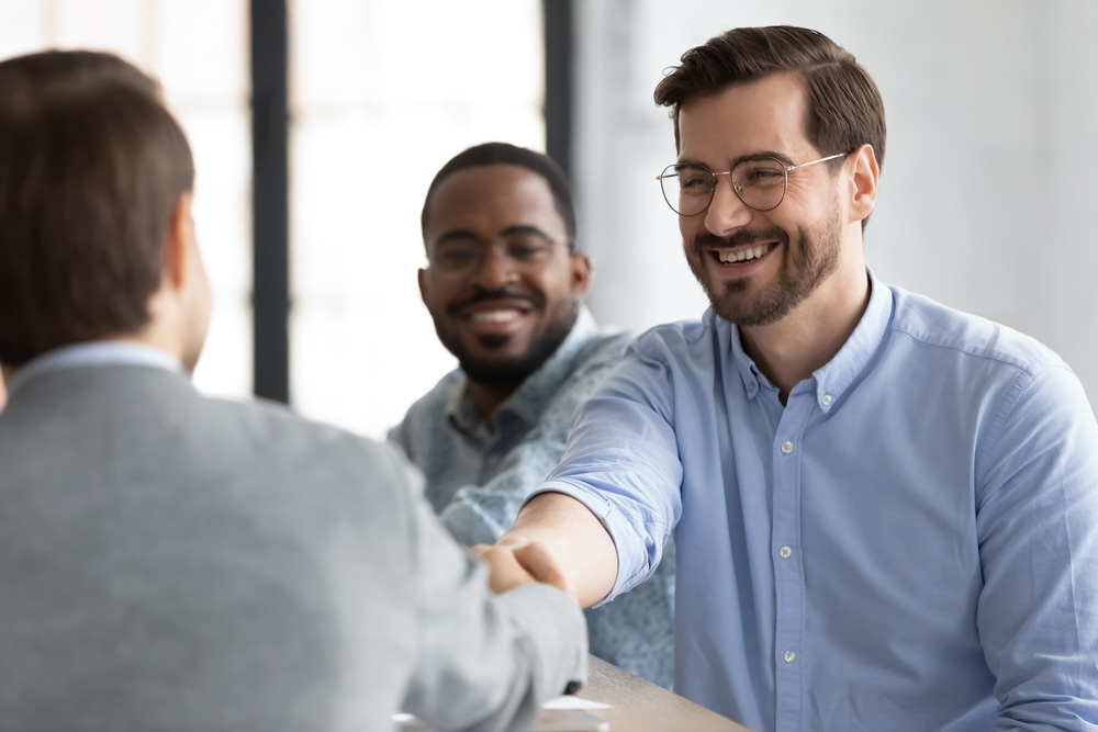 Three men meeting at a conference table with two men shaking hands.