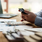 guy working on phone at desk with calculator and papers.