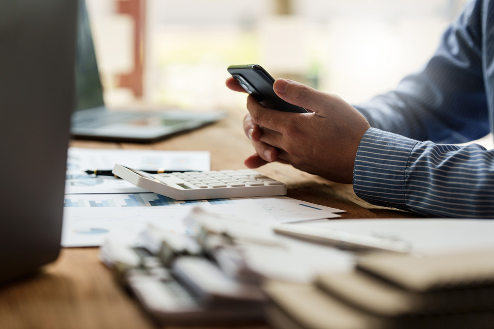 guy working on phone at desk with calculator and papers.